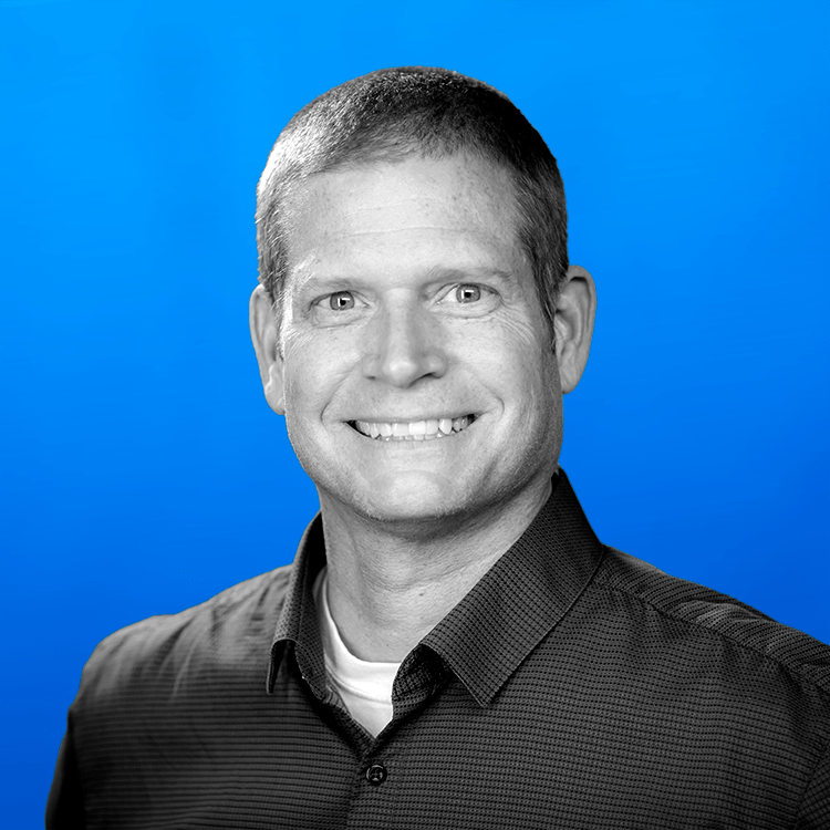 Headshot photo of Jonas Fitness' Software Development Manager, Mike Bevins, standing in front of a blue background.
